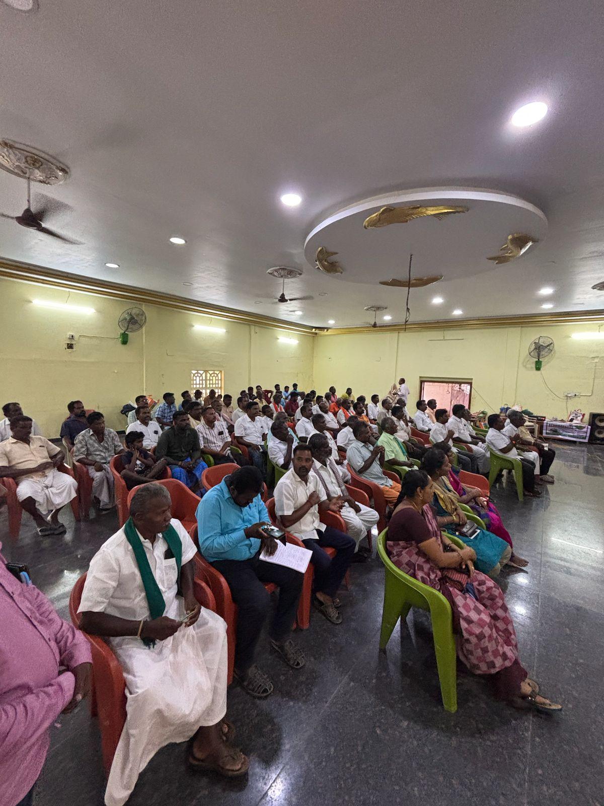 A community assembly seated in a hall, listening to a speaker.
