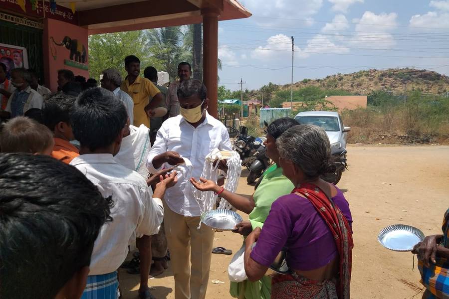 A Foundation volunteer distributing supplies to elderly community members outside a village hall.