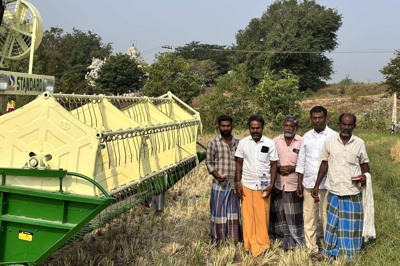 Five farmers standing beside a combine harvester at the edge of a field.