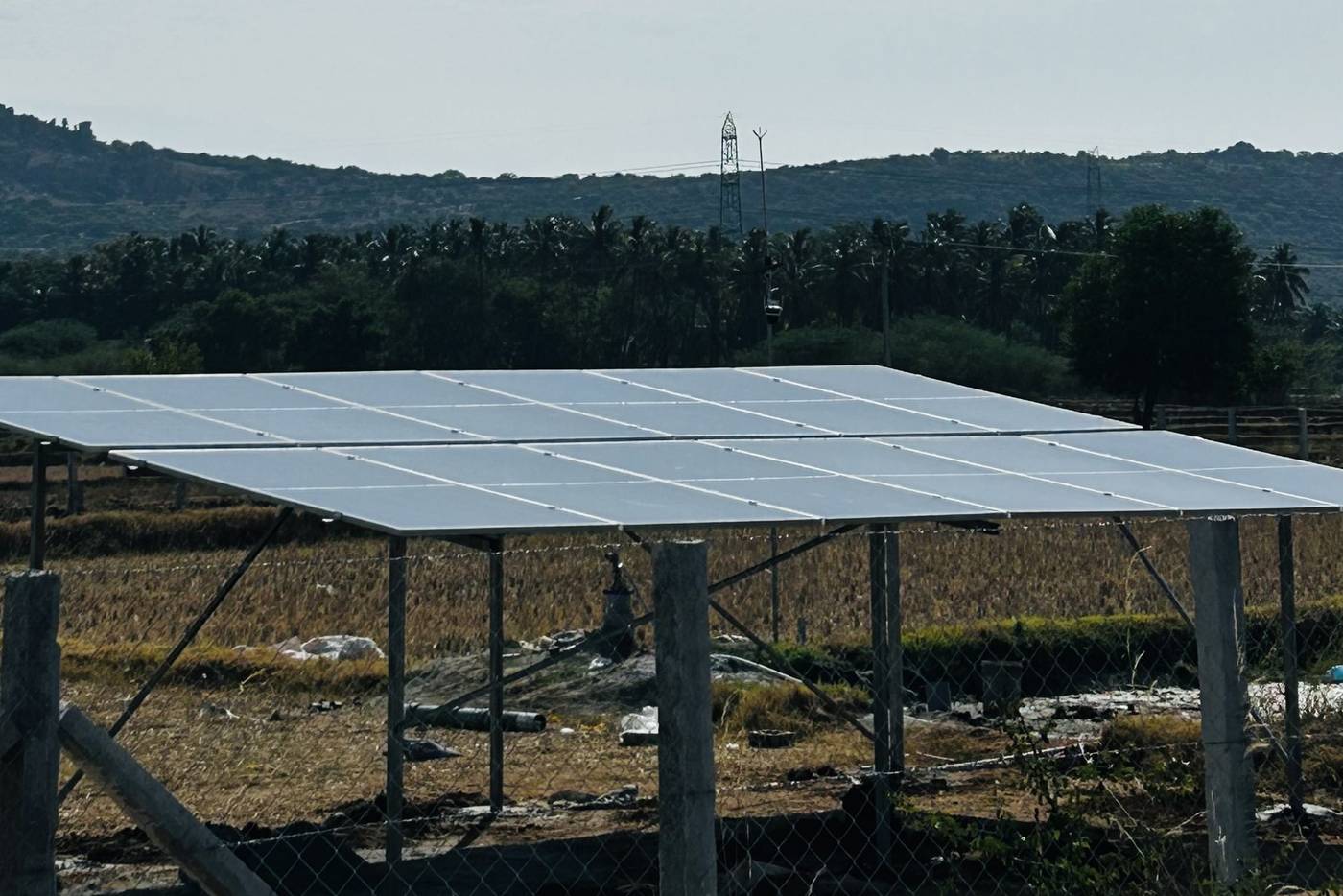 A ground-mounted solar array in open farmland, hills on the horizon.