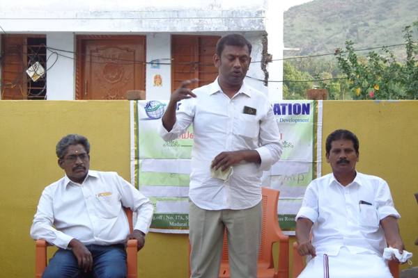 Addressing a village programme in the open, alongside community representatives.